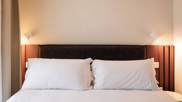 A bed with white bedding, a dark headboard, and two wall-mounted light fixtures.