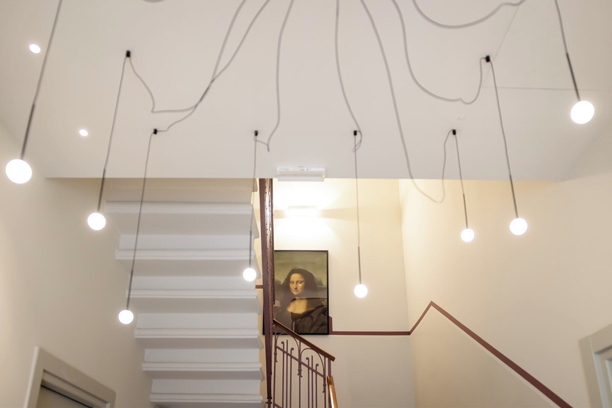 Una escalera con un cuadro encima, un techo con cableado expuesto y luces colgantes.