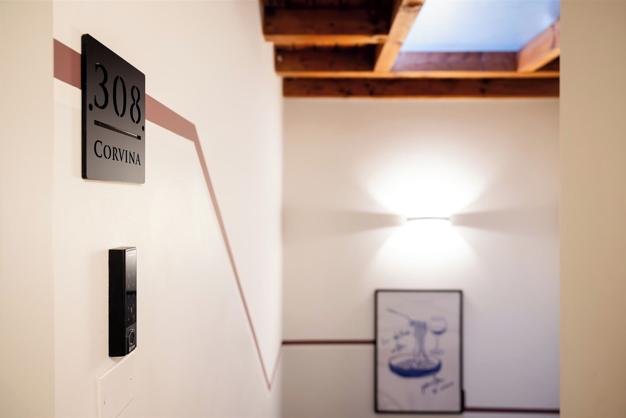 A room with a sign reading '308 Corvina,' a door with a keypad, and a framed artwork on the wall.