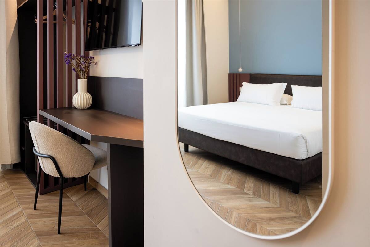 Una habitación de hotel con cama, escritorio, silla, televisor y espejo.
