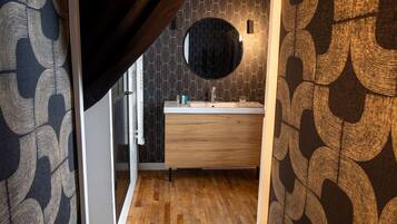 Un baño con un mueble de tocador de madera, un espejo redondo y un papel tapiz estampado.