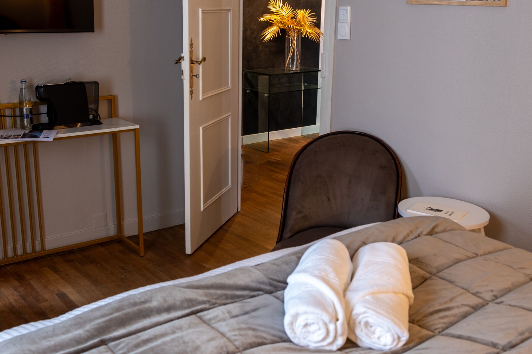 Quarto de hotel com cama, escrivaninha, cadeira, televisão e porta para outro cômodo.