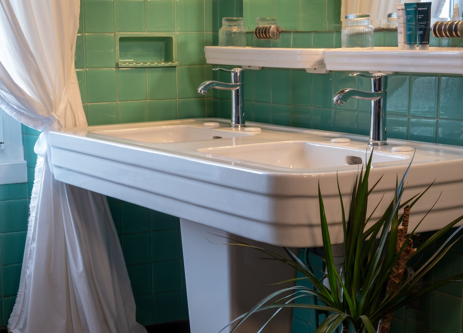A bathroom with a white sink, green tiles, and a mirror above it.