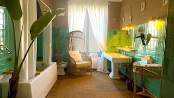 Une salle de bain avec une baignoire, un fauteuil en osier, un lavabo et un miroir.