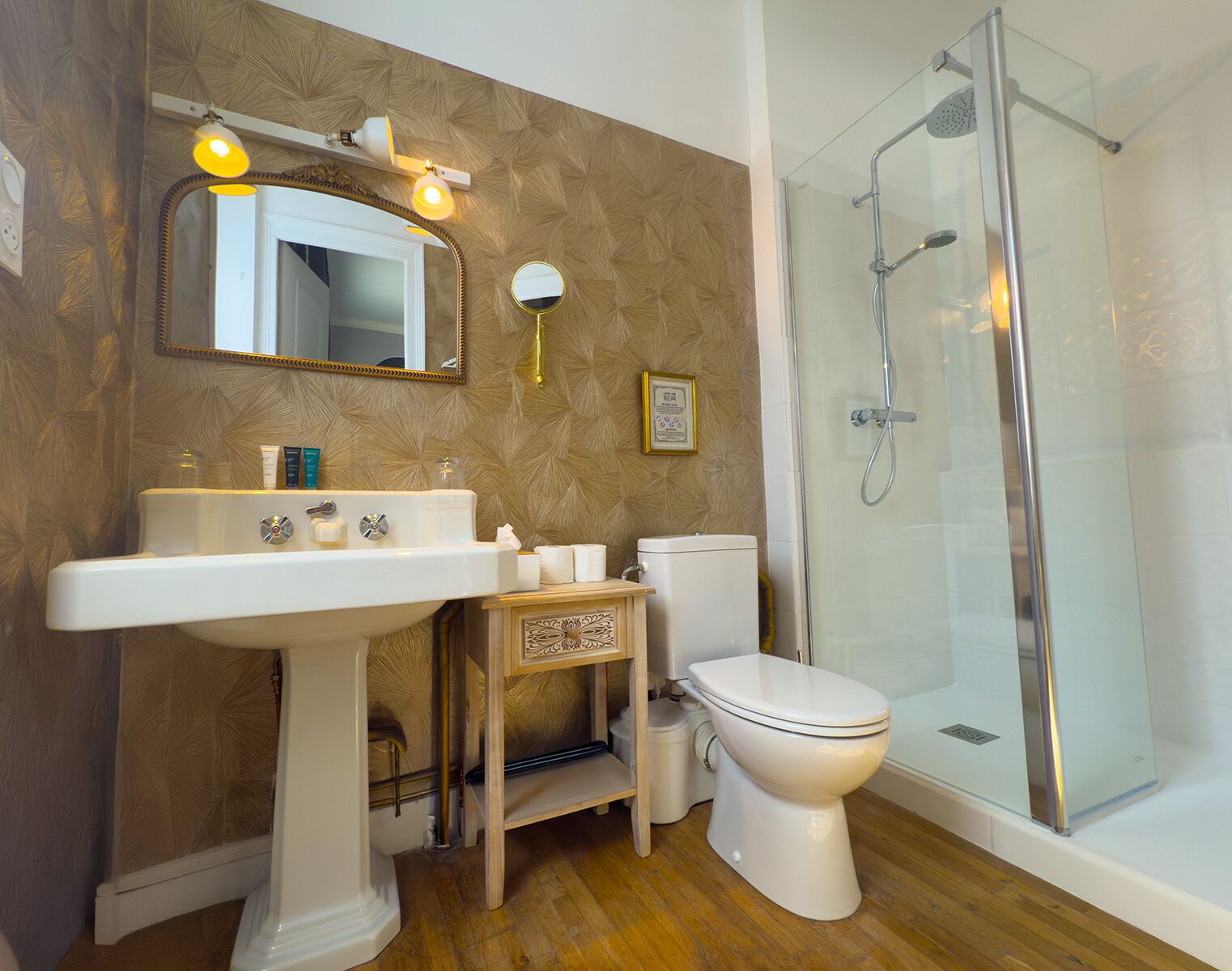 Un baño con lavamanos pedestal, inodoro, ducha con cerramiento de vidrio y espejo con iluminación.