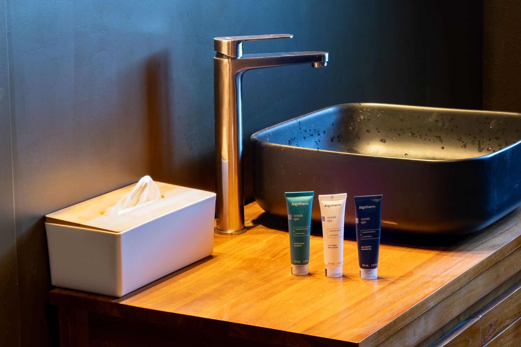 A bathroom sink with a tissue box and three bottles of Algotherm body cream.