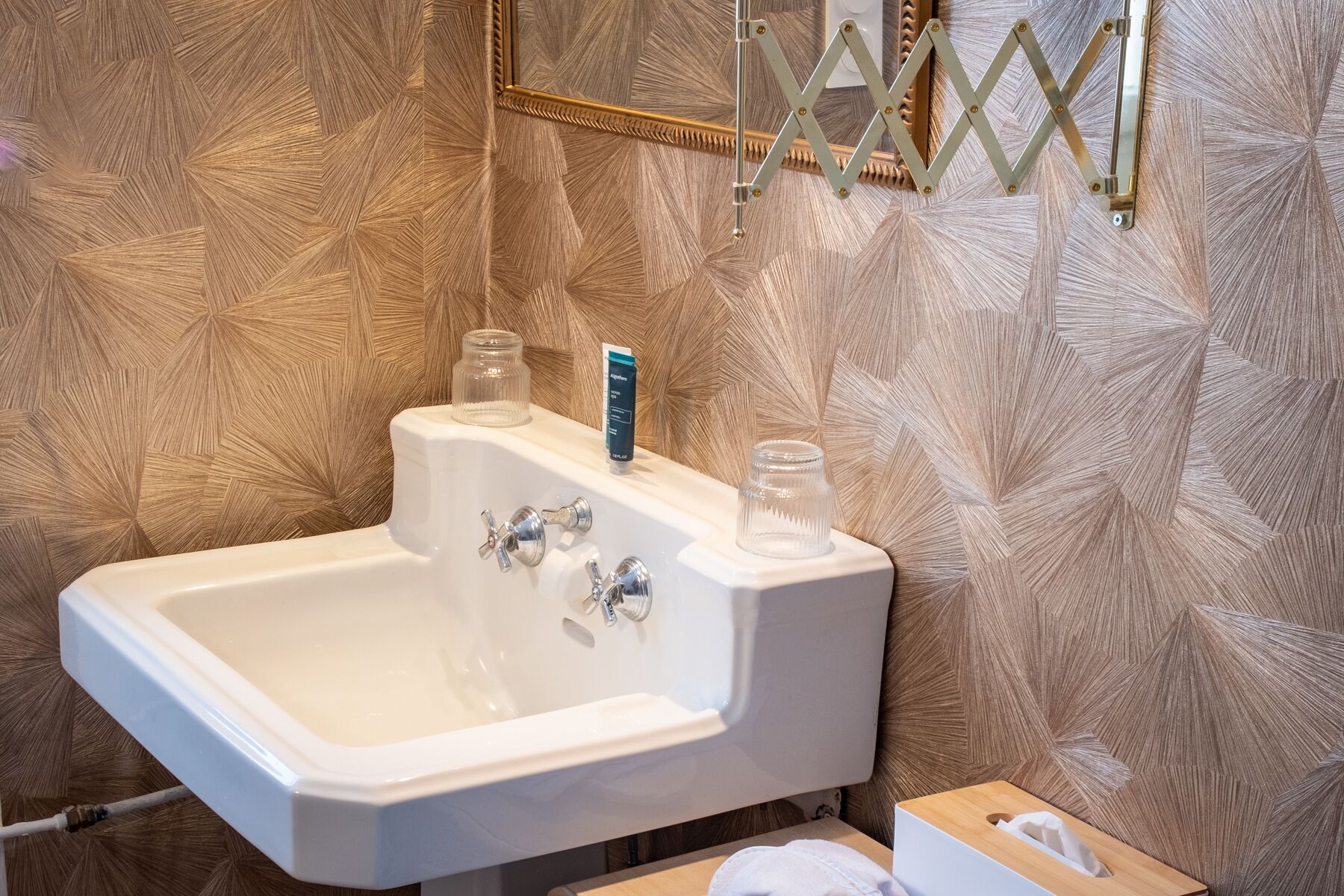 A bathroom with a white sink, two glass bottles, and a tissue box on a wooden surface.