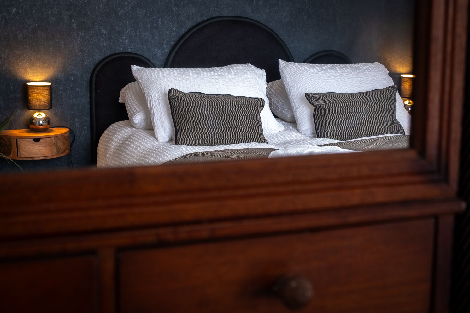A neatly made bed with white and patterned pillows, a wooden headboard, and bedside lamps.
