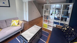 A living room with a sofa, a small table, a storage unit, and a staircase. - Westmeads wings. 5 minutes walk to the harbour and close to town and beach (Whitstable)