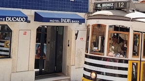 Un tranvía amarillo con el número 581, pasando frente a un edificio con fachada de azulejos azules y un cartel que dice 'Hotel Dalma Baixa'.