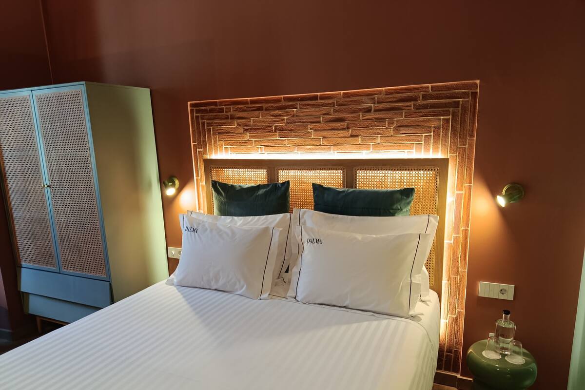 Une chambre d’hôtel avec un lit, deux oreillers, une table de chevet verte et une poubelle verte.
