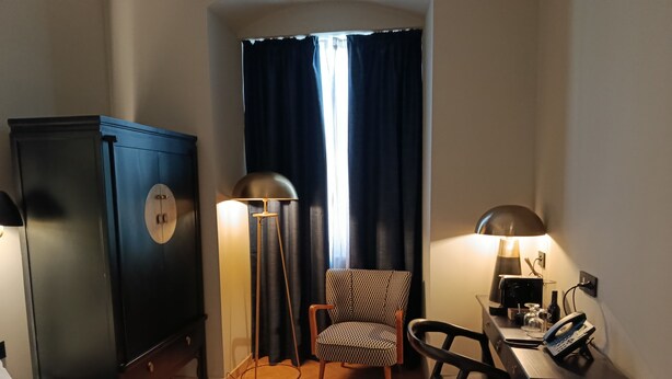 Une chambre d’hôtel comprenant un lit, un bureau avec un téléphone, une chaise, une armoire et une lampe sur pied.