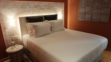 A neatly made bed with white bedding and pillows labeled "DALMA" in a room with a patterned wall and a decorative panel.