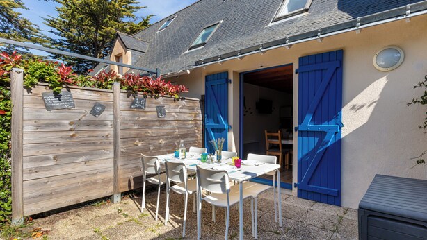 Une terrasse avec une table et des chaises, une clôture en bois et un bâtiment aux volets bleus.