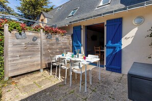 Un patio con una mesa y sillas, una valla de madera y un edificio con contraventanas azules.