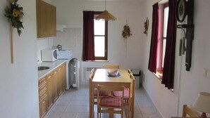A compact kitchen with a dining table, wooden cabinets, a microwave, and a window with curtains. - Serene Mansion With Pool (Starkov)