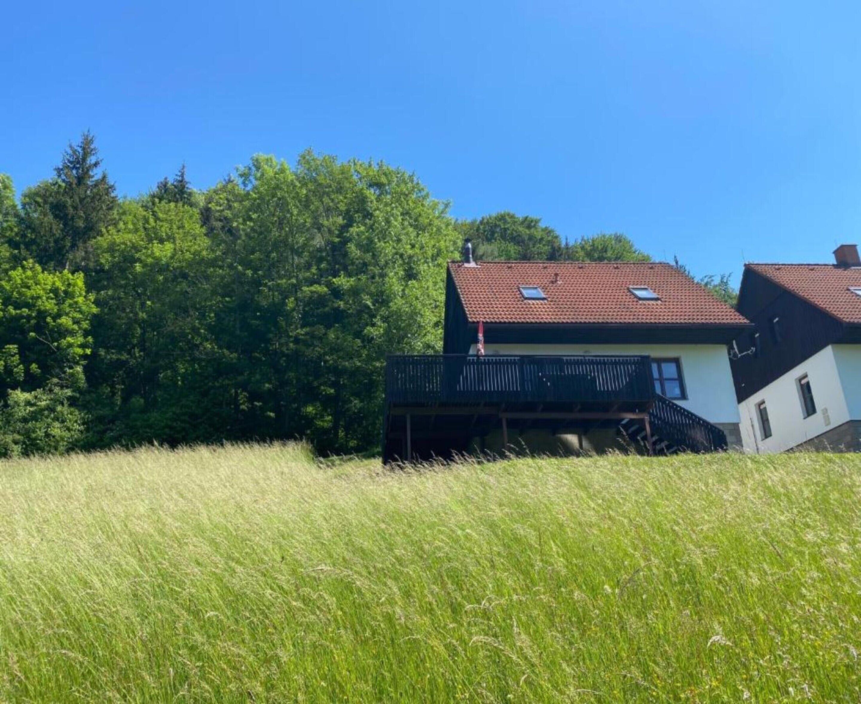 A house with a balcony, surrounded by tall grass and trees.