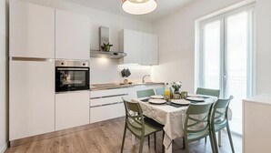 Een moderne keuken met witte kasten, een inbouwoven en een eethoek met een tafel gedekt voor twee personen.