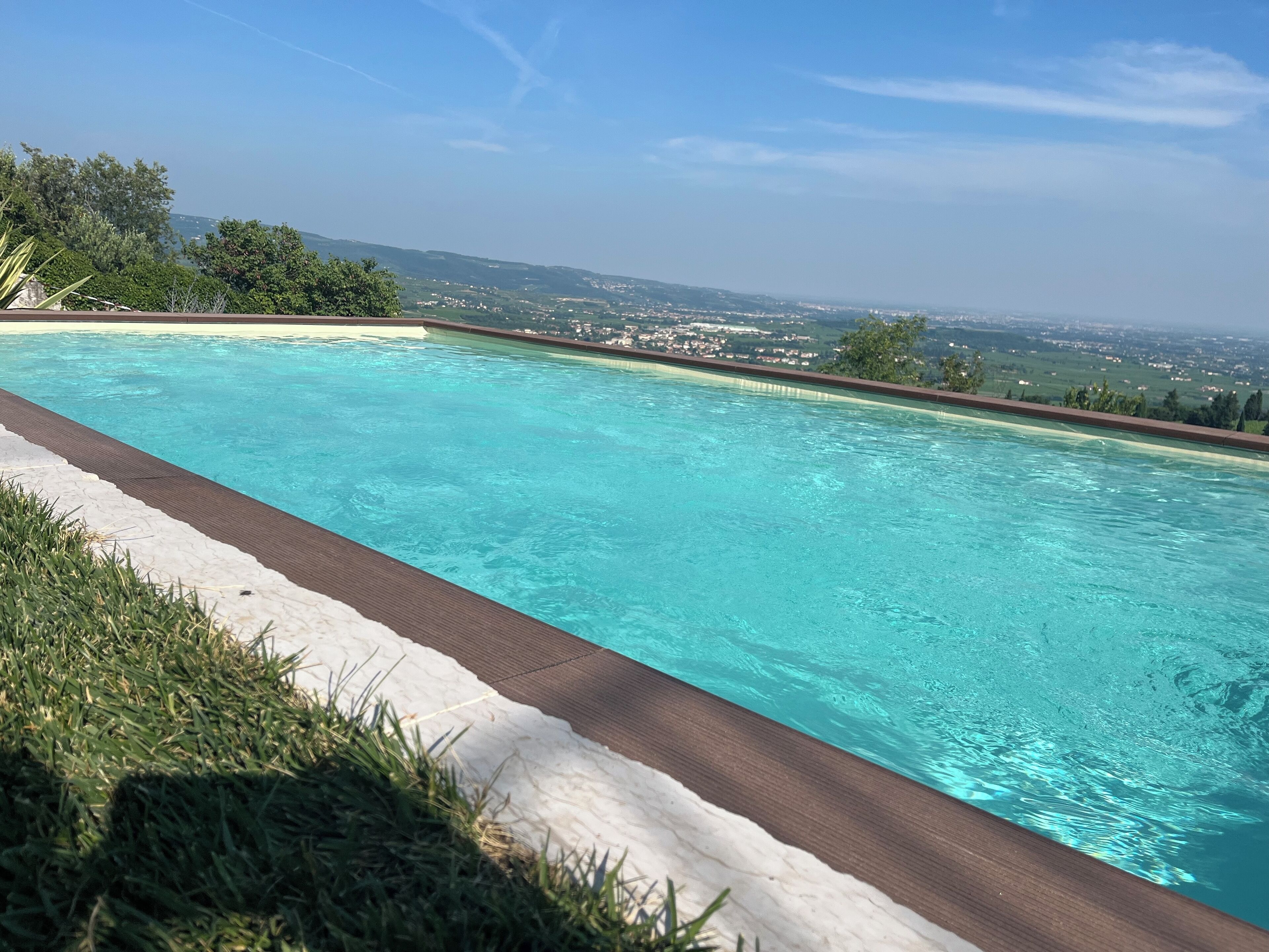 A swimming pool with clear blue water, surrounded by a white deck and green grass.