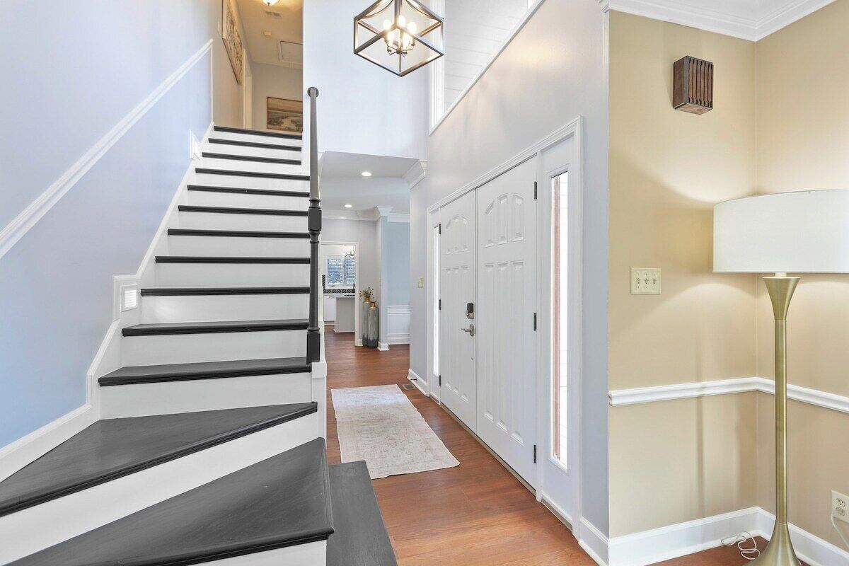 A staircase with black and white steps leading to a landing, a white floor lamp, and a beige wall with a door.