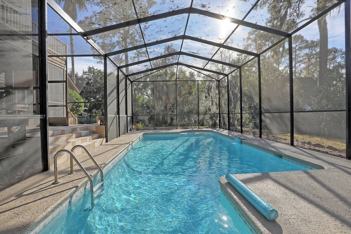 A swimming pool with a glass enclosure, surrounded by a concrete deck and steps leading to a house.