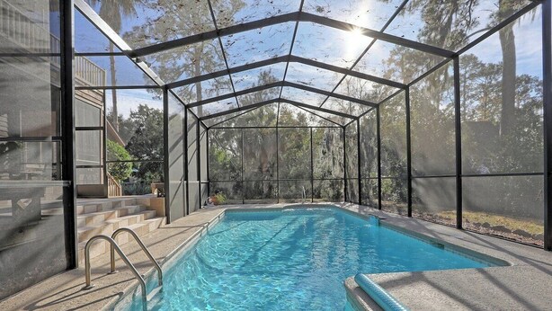 A swimming pool with a glass enclosure, surrounded by a concrete deck and steps leading to a house.