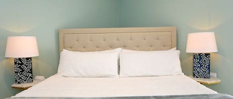 Una cama con cabecera capitonada, dos lámparas de noche con motivos de hojas y una colcha blanca.