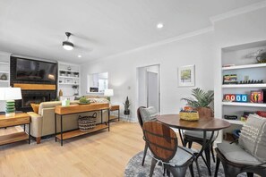 Un salon moderne avec une cheminée, un coin repas doté d’une table ronde et une bibliothèque remplie de livres et d’objets décoratifs.