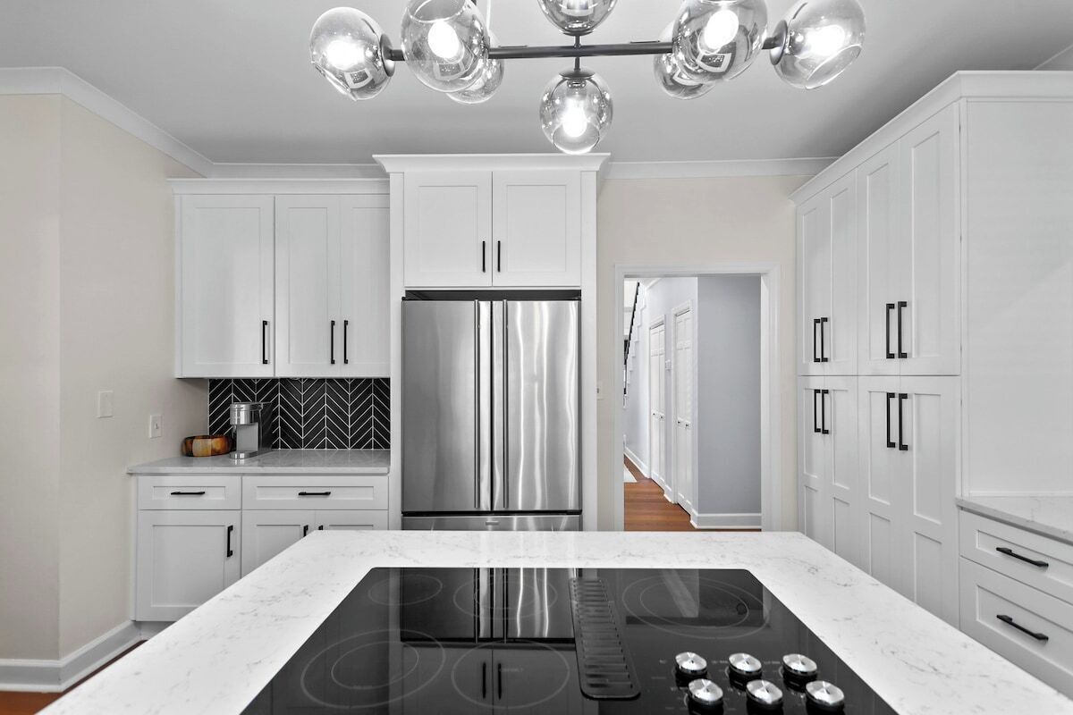 Una cocina moderna con armarios blancos, un refrigerador de acero inoxidable, una cocina por inducción negra y un salpicadero con motivo de espiga.