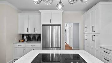 Una cocina moderna con armarios blancos, un refrigerador de acero inoxidable, una cocina por inducción negra y un salpicadero con motivo de espiga.
