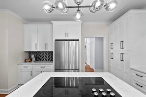 A modern kitchen with white cabinetry, a stainless steel refrigerator, a black induction cooktop, and a herringbone-patterned backsplash.
