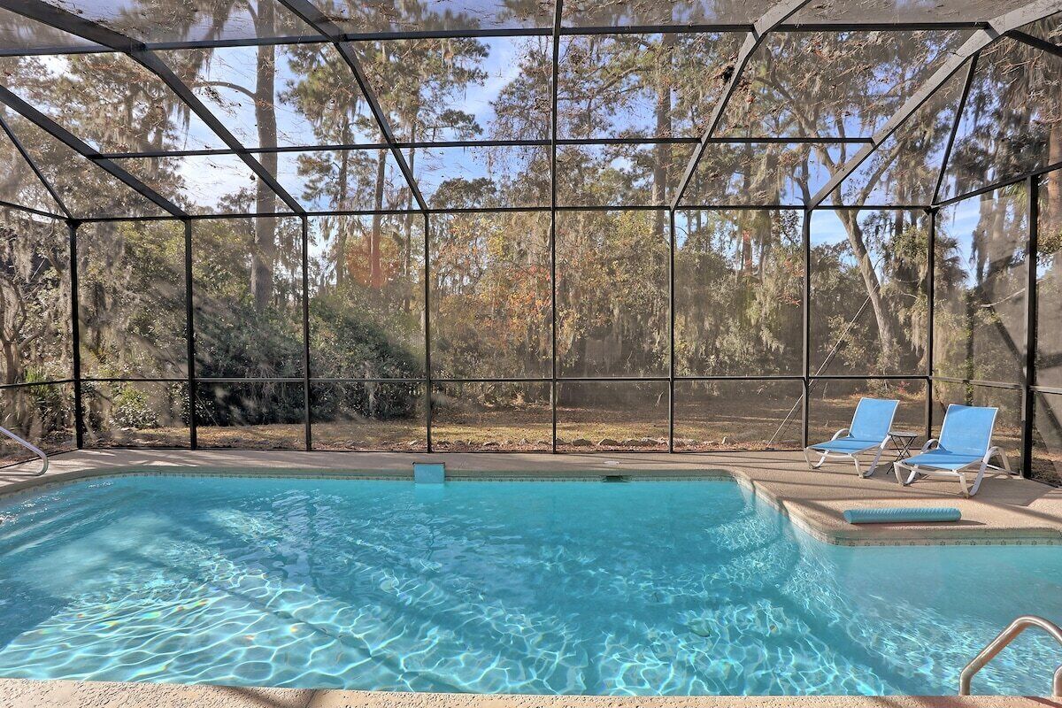 Une piscine intérieure à l’eau claire, entourée d’une structure en verre, et deux chaises longues.
