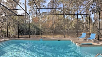 Une piscine intérieure à l’eau claire, entourée d’une structure en verre, et deux chaises longues.