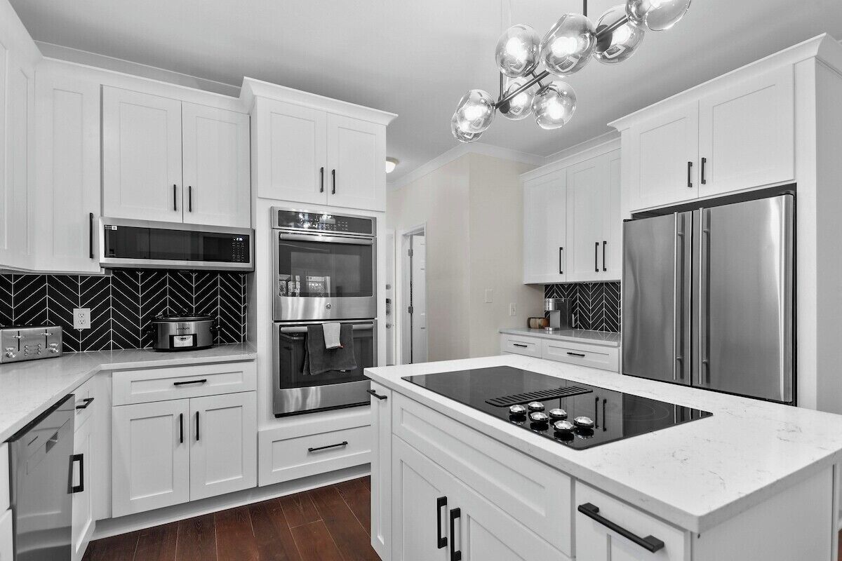 A modern kitchen with white cabinetry, stainless steel appliances, and a black and white backsplash.