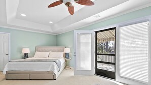 A bedroom with a bed, bedside lamps, a ceiling fan, and a view through a door to an outdoor area. - Pool Oasis by Tybee & Downtown Savannah (Savannah)