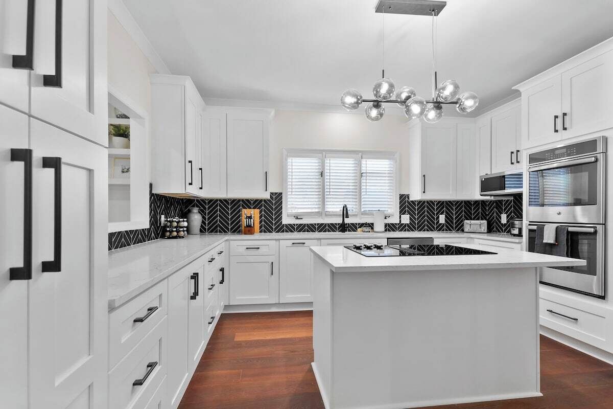 Une cuisine moderne avec des meubles blancs, un îlot central et un dosseret en motifs chevrons noir et blanc.