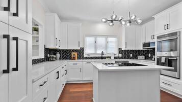 Une cuisine moderne avec des meubles blancs, un îlot central et un dosseret en motifs chevrons noir et blanc.