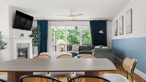 A modern living room with a dining area, large windows, and a fireplace. - Boho Luxe Stay Game Room, Fire Pit & Playground (Raleigh)