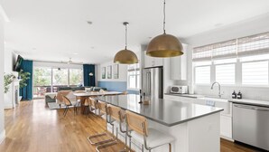 A modern kitchen with a central island, stainless steel appliances, and a dining area with bar stools. - Boho Luxe Stay Game Room, Fire Pit & Playground (Raleigh)