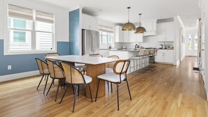 A modern kitchen with a central island, white cabinetry, and a dining area with six chairs. - Boho Luxe Stay Game Room, Fire Pit & Playground (Raleigh)