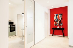 A modern kitchen with a built-in oven, a white dining area, and a red accent wall with abstract art.
