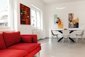 A modern living room with a red sofa, a dining table with chairs, and abstract art on the walls.