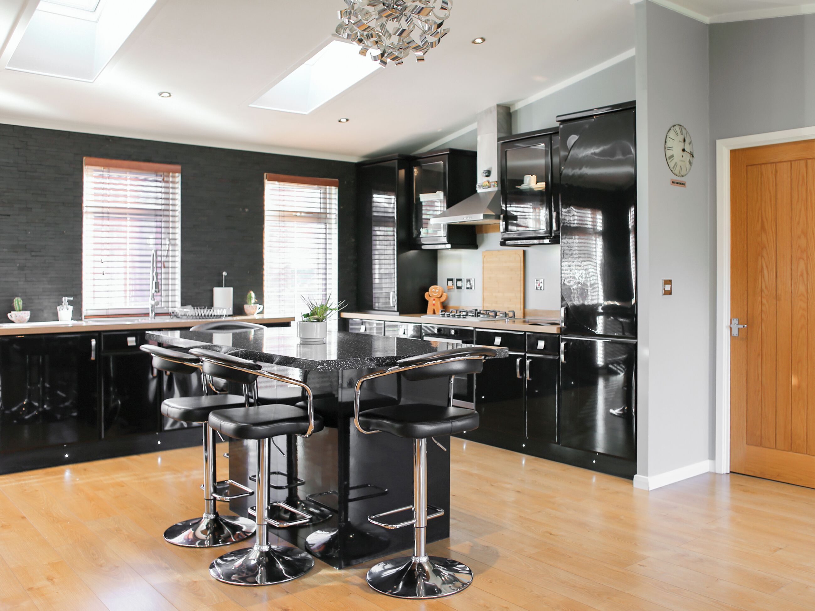 Een moderne keuken met een centraal eiland, zwarte barkrukken en een houten vloer.