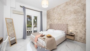 A bedroom with a large bed, a nightstand, a mirror, and a view of the outdoors. - Kosmas Apartments (Corfu)