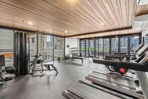 A gym with cardio equipment, weight machines, and a large window overlooking a cityscape.