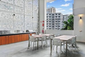 A modern kitchen with a large island, dining area with tables and chairs, and a view of buildings through a window.