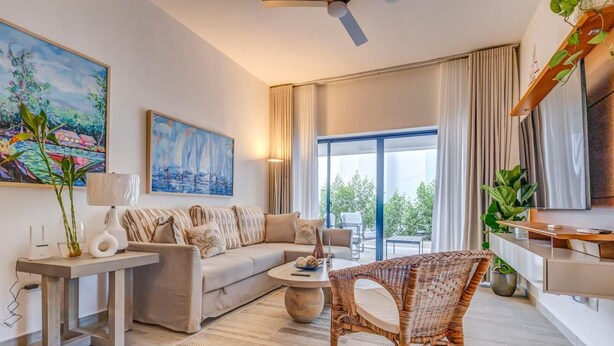 A modern living room with a sofa, a wicker chair, a coffee table, and a TV. - ENJOY THIS BEAUTIFUL APARTMENT IN PUNTA CANA (Higüey)