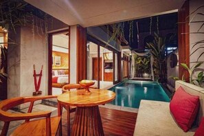 An indoor pool area with a wooden table and chairs, a red cushion, and a view of the pool. - Sampatti Villas (Bali)