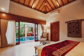 A bedroom with a bed, a chair, a lamp, a door, and a view of a pool. - Sampatti Villas (Bali)