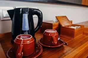 A wooden table with a black electric kettle, two red cups, and a box of sugar. - Sampatti Villas (Bali)